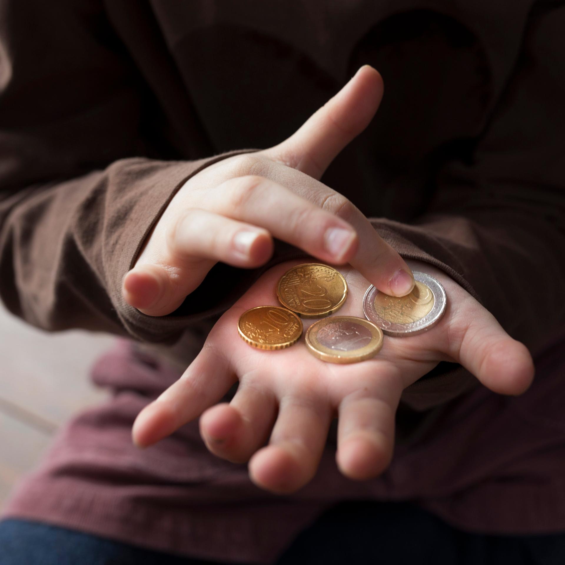 Ein Kind zählt kleines Taschengeld auf seiner Hand.