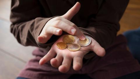 Ein Kind zählt kleines Taschengeld auf seiner Hand.