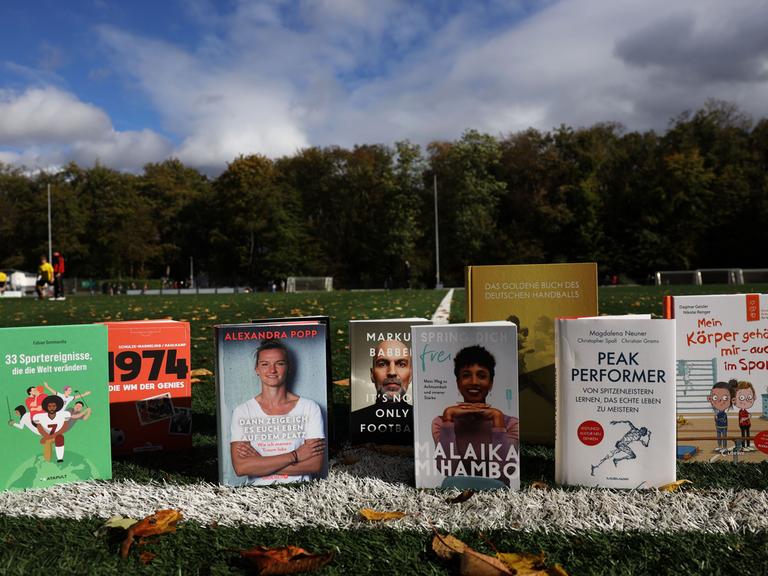 Die Sportbücher des Jahres 2023 stehen auf einem Fußballfeld an der Seitenlinie aufgereiht.