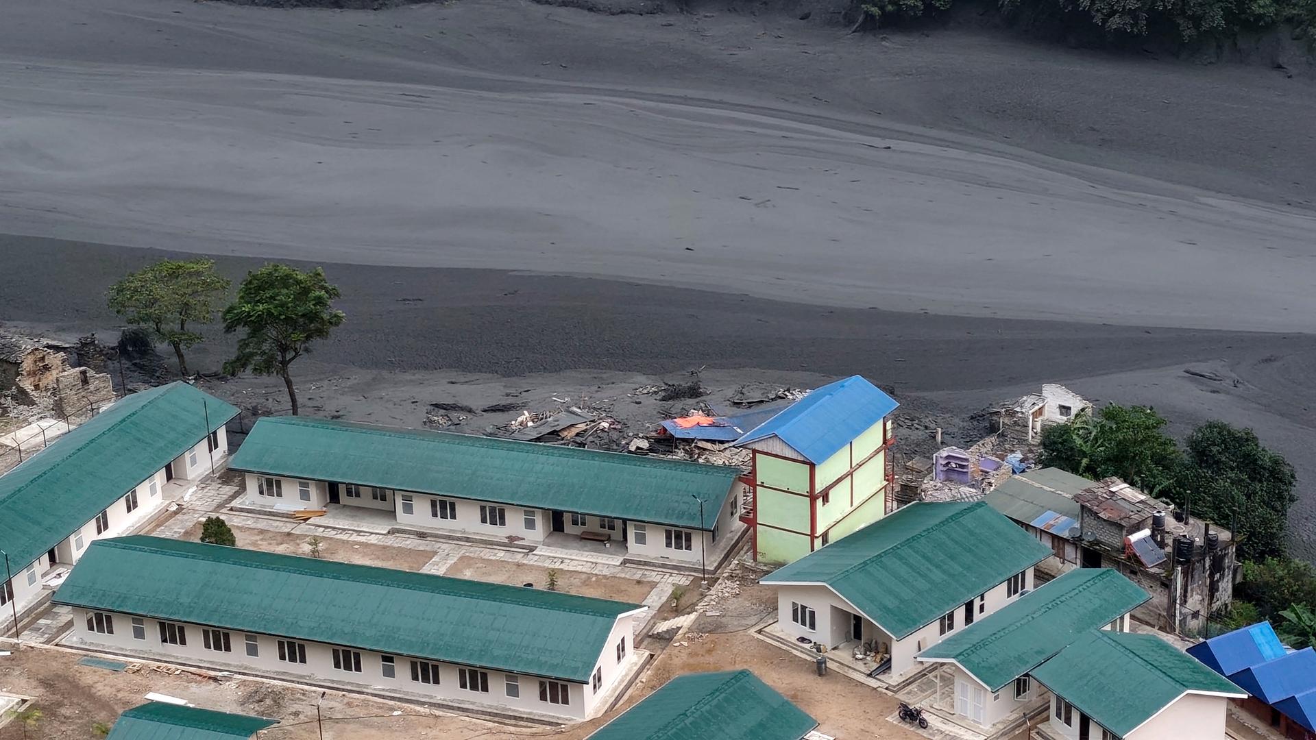 Im Vordergrund sieht man mehrere Gebäude eines Wasserkraftwerks; im Hintergrund sieht man den Fluss Budhigandaki, der massiv angeschwollen ist.