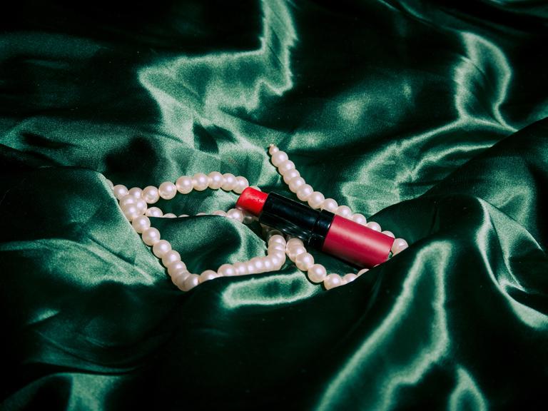 Ein Lippenstift und eine Perlenkette liegen auf einem grünen Tuch.