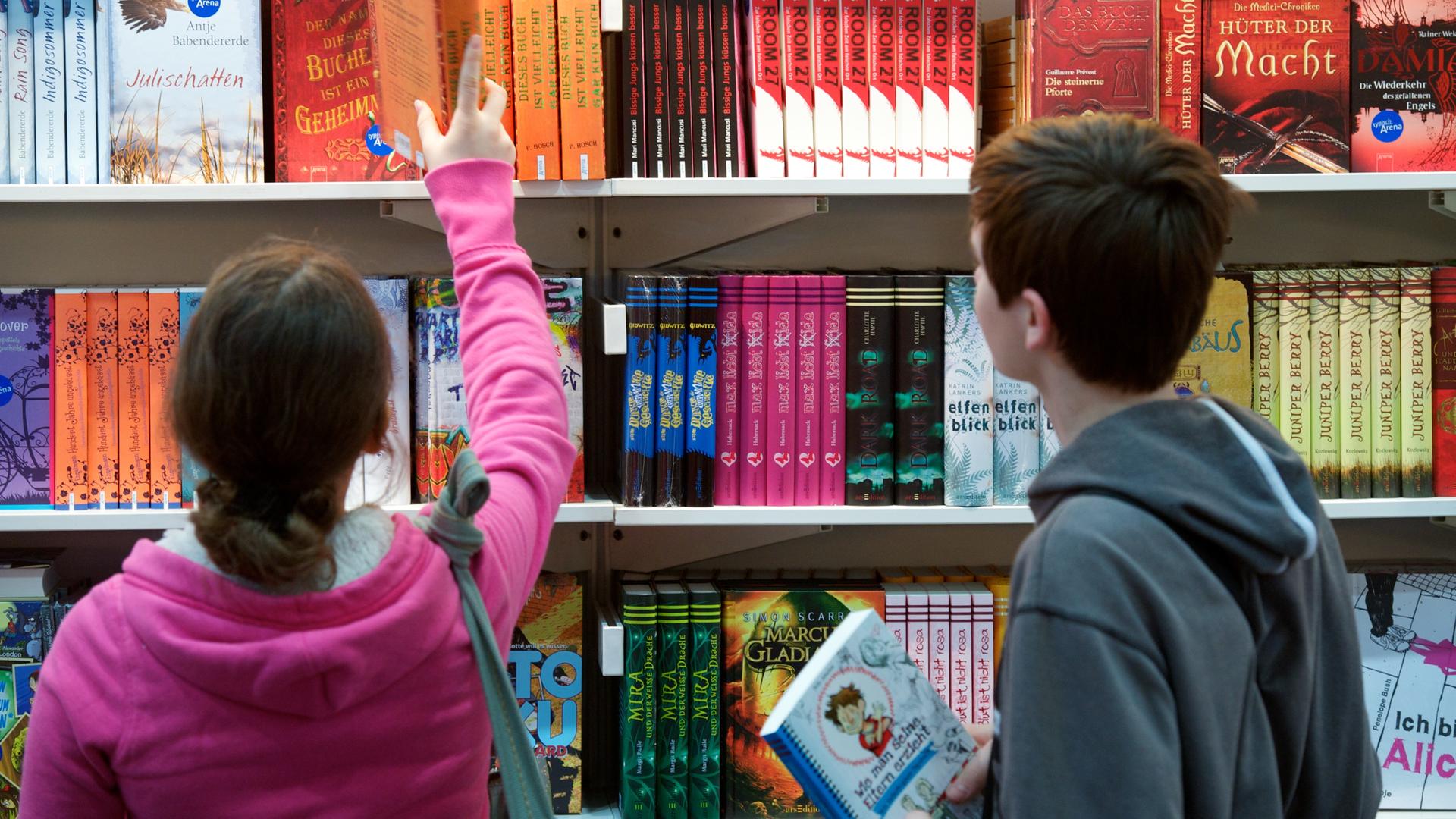 Kinder schauen sich Bücher in einem Regal an. 