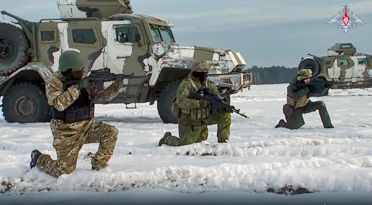 Drei Soldaten knien vor einem Militärfahrzeug im Schnee und zielen mit ihren Gewehren nach vorne.