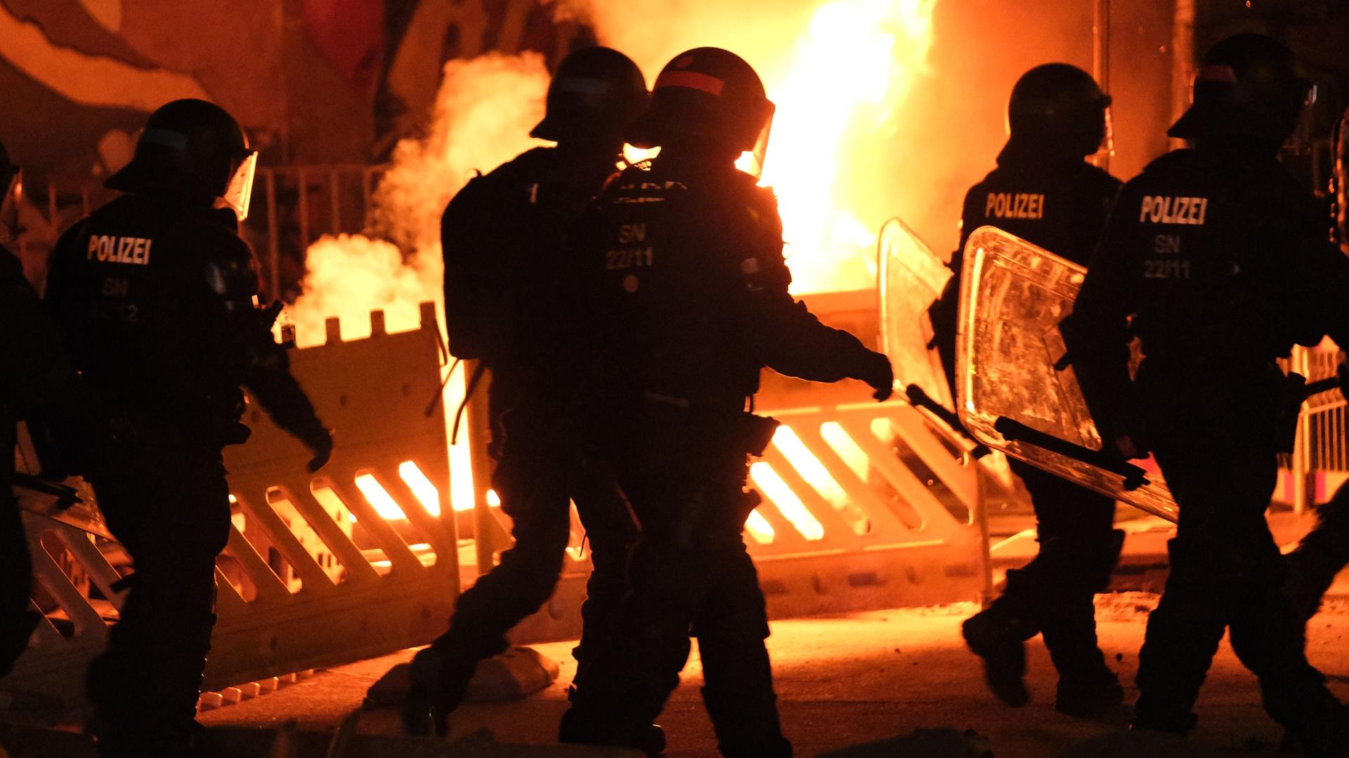 Polizisten gehen an einer brennenden Barrikade im Leipziger Stadtteil Connewitz vorbei, wo es zu Ausschreitungen gekommen ist. 