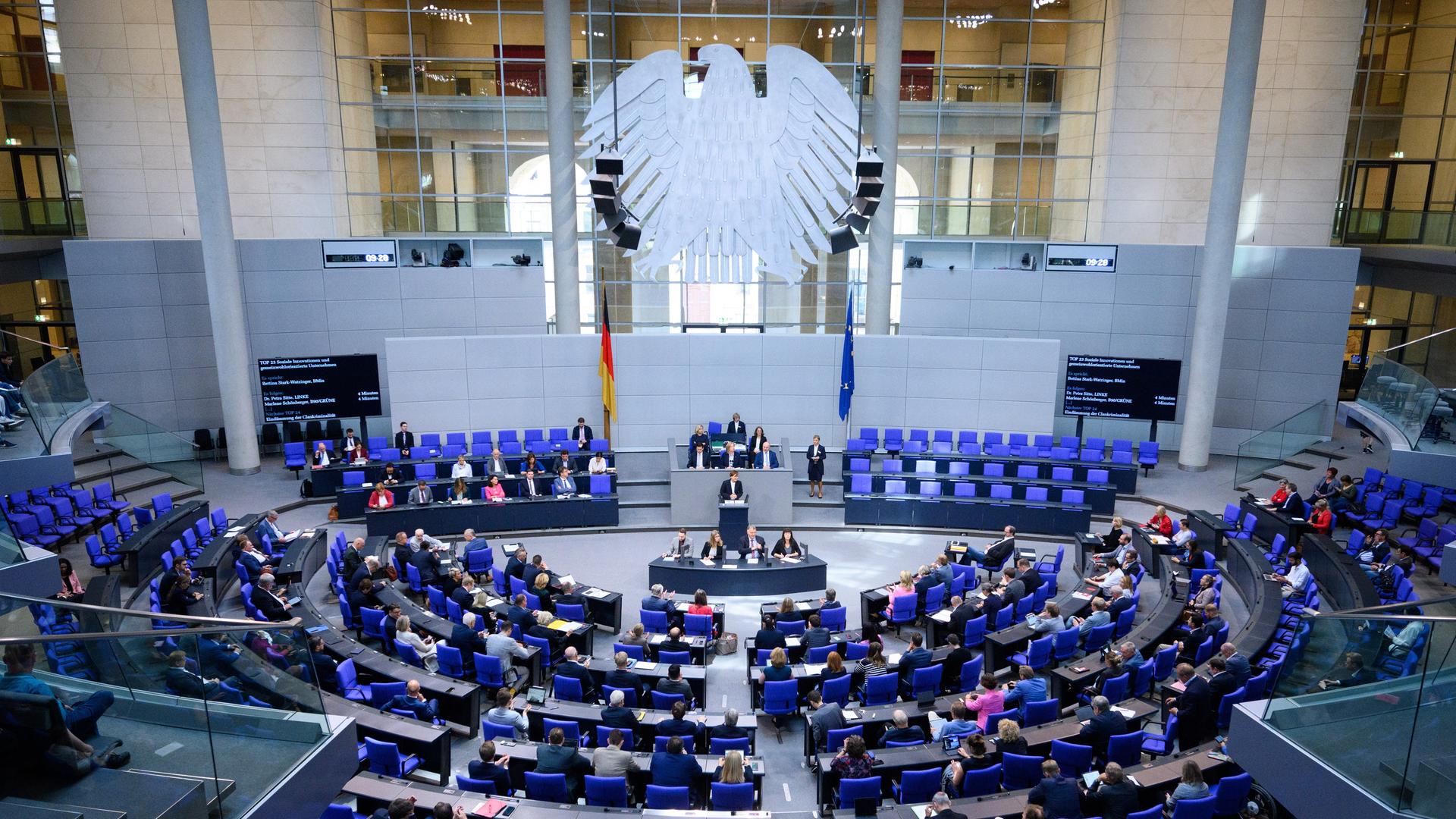Plenarsitzung im Deutschen Bundestag. Links eine Deutschlandfahne, rechts eine der EU, dazwischen das Rednerpult. Drumherum die Sitze der Abgeordneten.