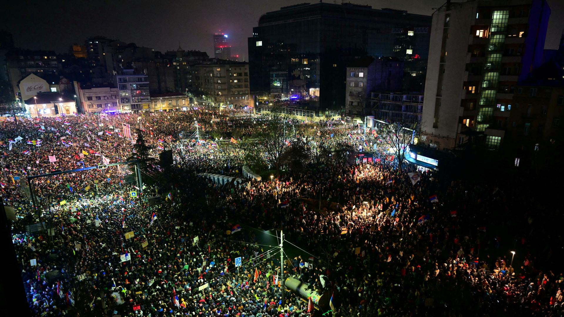 Die Aufnahme zeigt eine Großdemonstration in Belgrad aus der Vogelperspektive. Tausende Demonstranten stehen im Dunkeln auf einem Platz.