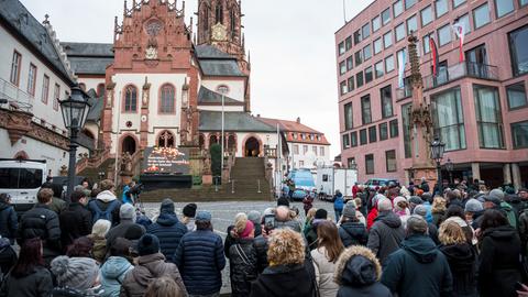 Menschen schauen auf einen Bildschirm vor der Kirche St. Peter und Alexander in Aschaffenburg, auf dem der Gedenkgottesdienst für die Opfer der Messerattacke vom vergangenen Mittwoch übertragen wird.