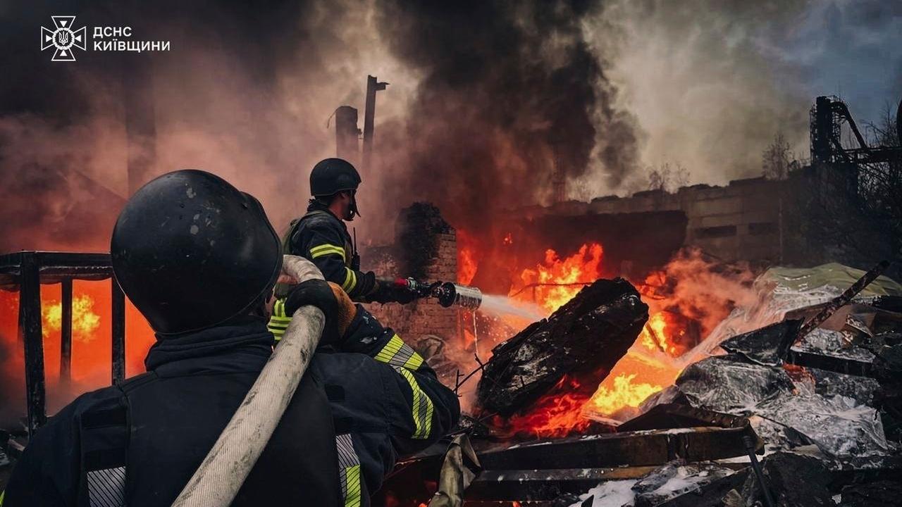 Zwei Feuerwehrmänner löschen den Brand an einem Gebäude.