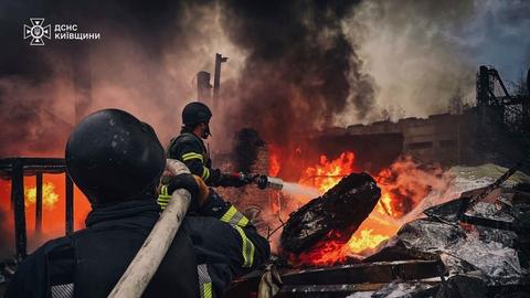 Zwei Feuerwehrmänner löschen den Brand an einem Gebäude.