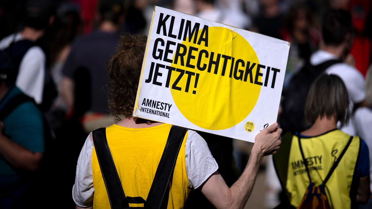 Eine Person bei einer von Amnesty International und der Fridays-For-Future-Bewegung organisierten Demonstration hält ein Schild in die Luft, auf dem "Klima Gerechtigkeit jetzt" steht.
