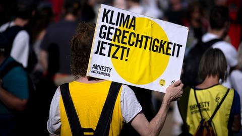 Eine Person bei einer von Amnesty International und der Fridays-For-Future-Bewegung organisierten Demonstration hält ein Schild in die Luft, auf dem "Klima Gerechtigkeit jetzt" steht.