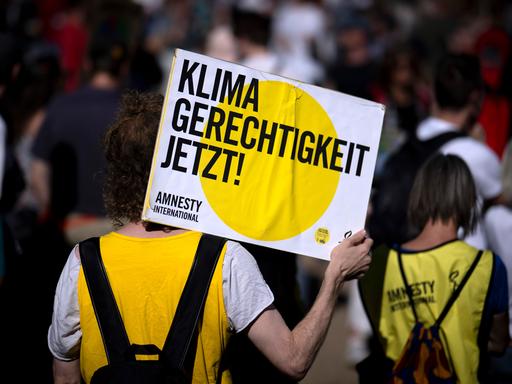 Eine Person bei einer von Amnesty International und der Fridays-For-Future-Bewegung organisierten Demonstration hält ein Schild in die Luft, auf dem "Klima Gerechtigkeit jetzt" steht.