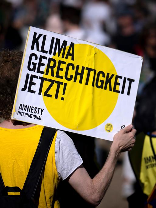 Eine Person bei einer von Amnesty International und der Fridays-For-Future-Bewegung organisierten Demonstration hält ein Schild in die Luft, auf dem "Klima Gerechtigkeit jetzt" steht.
