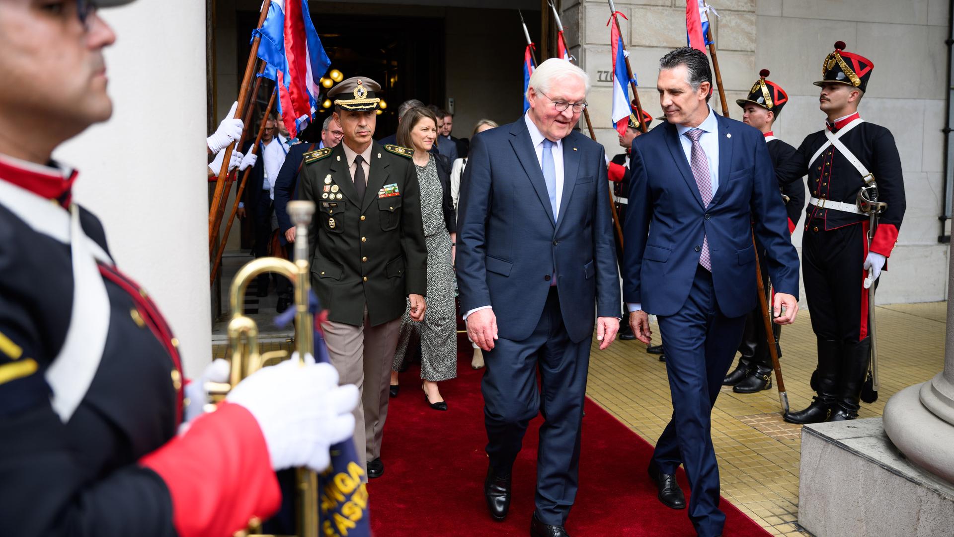 Bundespräsident Steinmeier läuft neben dem Präsidenten von Uruguay, Orsi, aus einem Gebäude. Hinter ihnen ist Entourage zu sehen, Soldaten stehen Spalier.