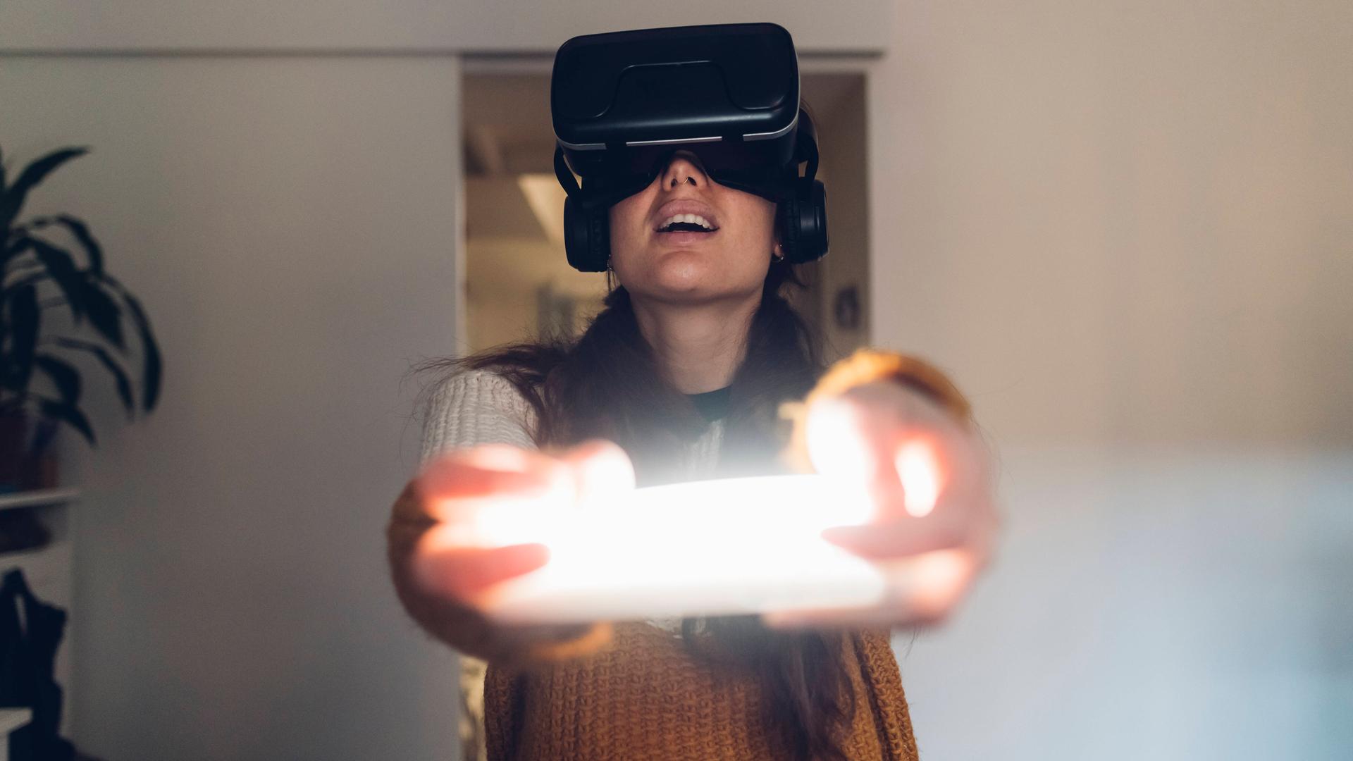 Eine Frau hält eine Virtual Reality Konsole und trägt Kopfhörer.