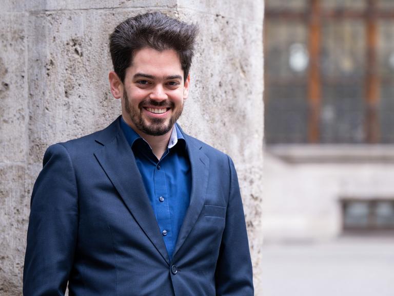 Lahav Shani, zukünftiger Chefdirigent der Münchner Philharmoniker, lehnt an einer Wand.