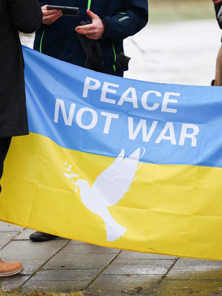 Während einer Demonstration halten zwei Personen eine blau-gelbe Fahne mit der Aufschrift "Peace - No war". 