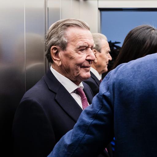 Altkanzler Gerhard Schröder (SPD) steht in einem Aufzug, neben ihm stehen weitere Personen.
