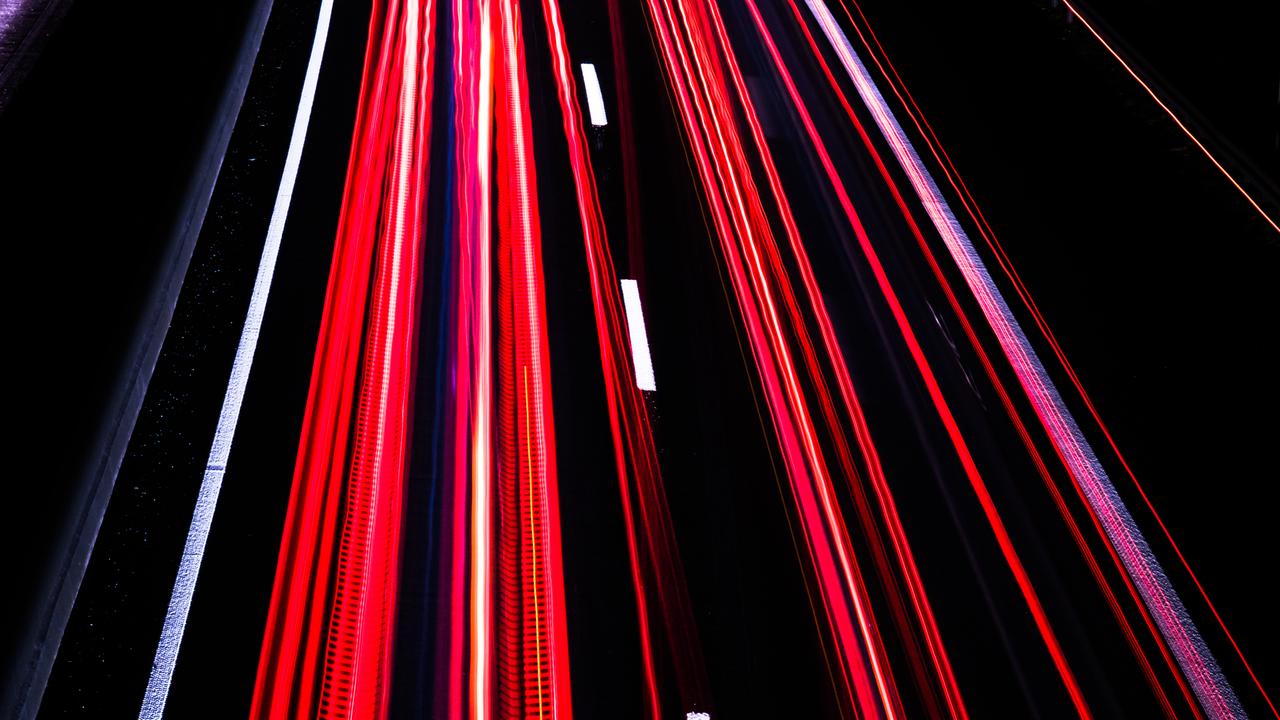 Langzeitbelichtung auf der Autobahn bei Nacht erzeugt rote und weiße Streifen auf schwarzem Asphalt