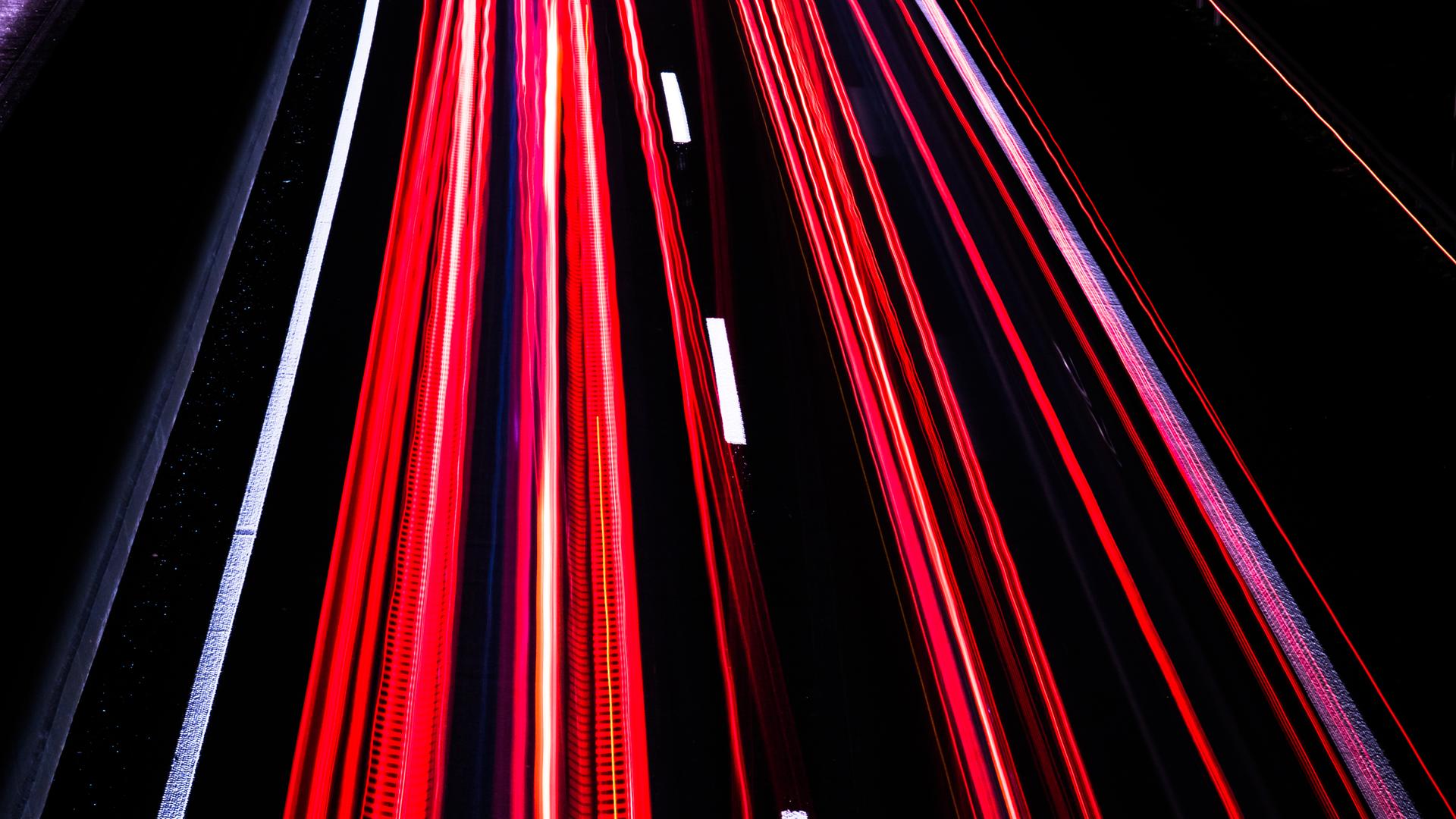 Langzeitbelichtung auf der Autobahn bei Nacht erzeugt rote und weiße Streifen auf schwarzem Asphalt