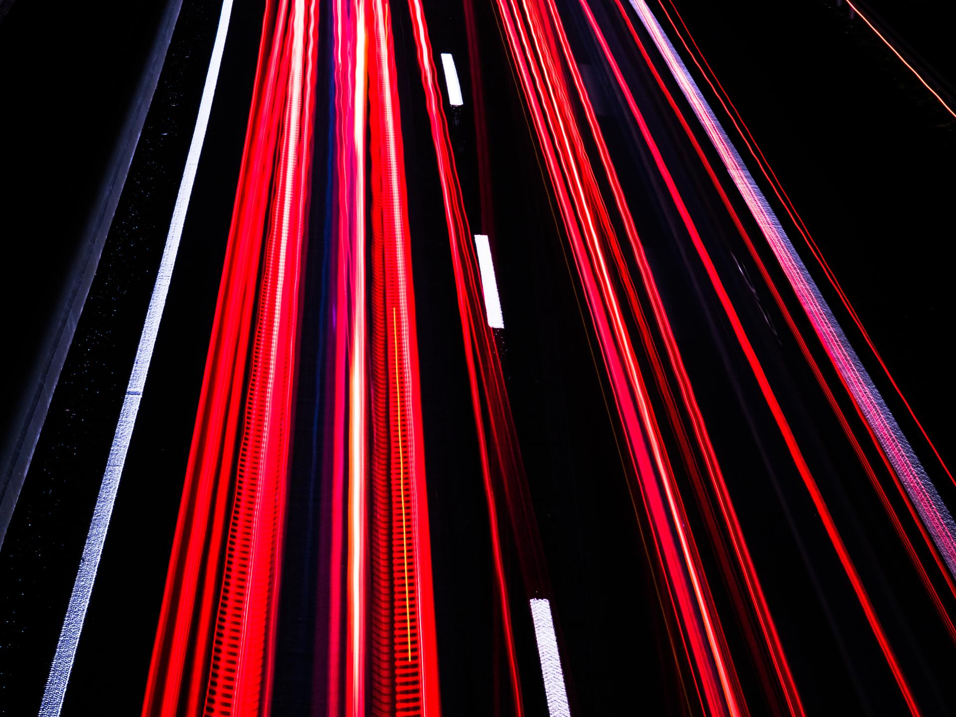 Langzeitbelichtung auf der Autobahn bei Nacht erzeugt rote und weiße Streifen auf schwarzem Asphalt