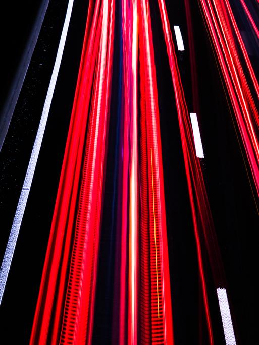Langzeitbelichtung auf der Autobahn bei Nacht erzeugt rote und weiße Streifen auf schwarzem Asphalt