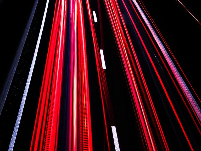Langzeitbelichtung auf der Autobahn bei Nacht erzeugt rote und weiße Streifen auf schwarzem Asphalt
