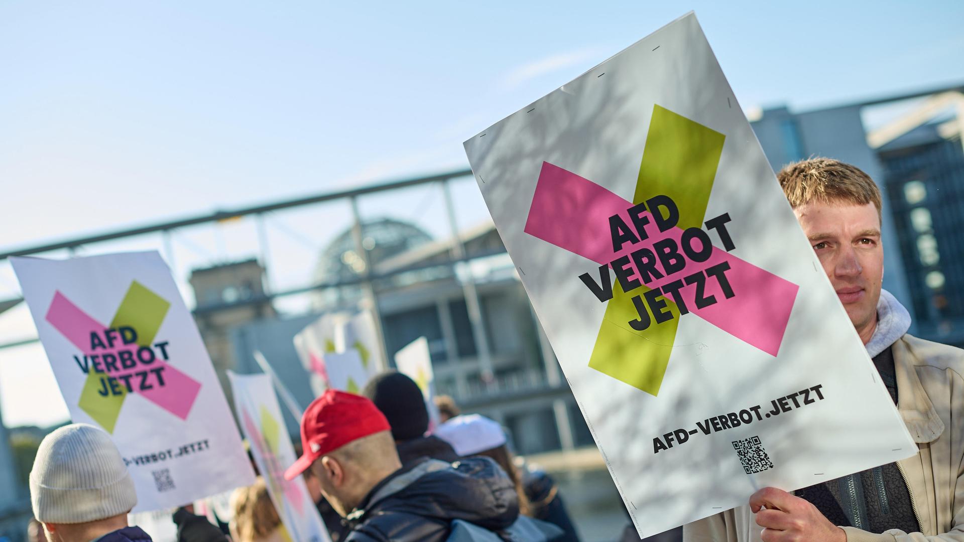 Mann hält Plakat auf Kundgebung, auf dem steht: "AfD Verbot Jetzt".