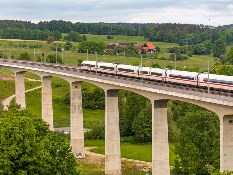 Bahnverkehr auf der Schnellfahrstrecke Nürnberg - Würzburg: Ein ICE fährt über eine hohe Brücke, eingerahmt von der Landschaft.