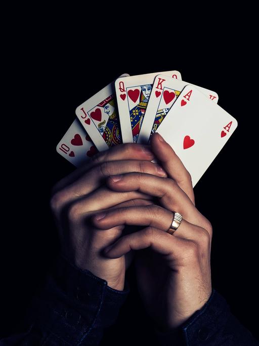 Zwei Hände fächern fünf Spielkarten auf und halten sie in die Kamera, Herz Zehn, Bube, Dame, König, Ass.