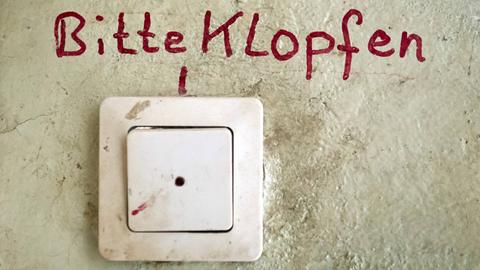 Unfassbare Vorkommnisse während eines Entmietungsprozesses - erzählt von betroffenen Bewohnern. Zu sehen: Eine Haustürklingel an einer Wand mit einem Schriftzug "Bitte klopfen" darüber. 