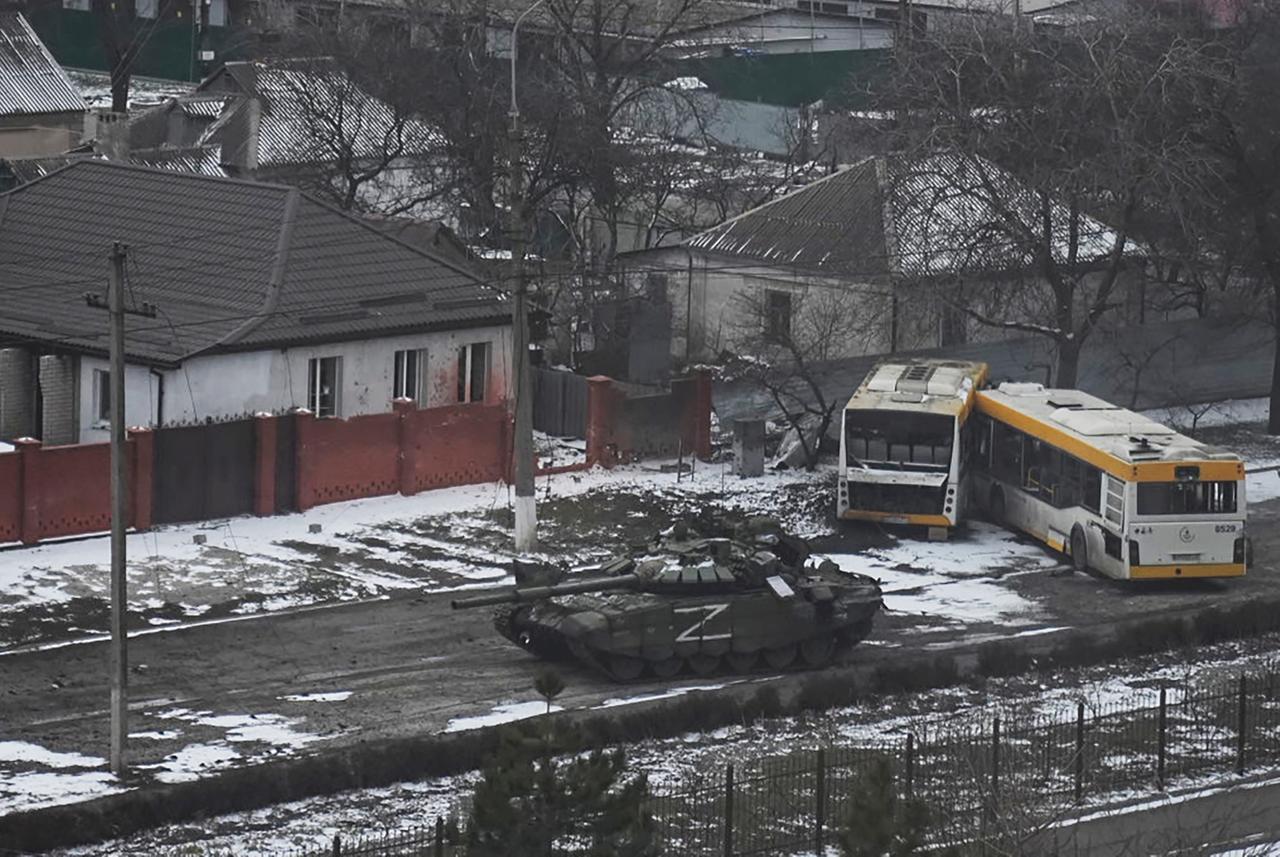 Ein Panzer der russischen Armee mit einem "Z" an der Seite bewegt sich durch eine Straße am Stadtrand von Mariupol, Ukraine. Daneben sind zwei zerstörte Busse zu sehen. 