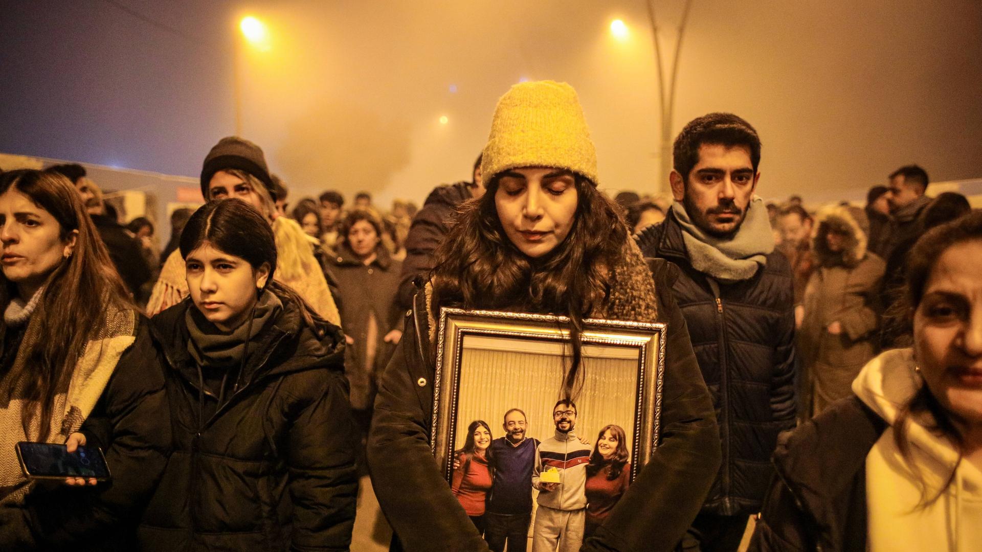 Eine Gruppe von Menschen erinnert in der türkischen Provinz Hatay den Opfern des Erdbebens vom Februar 2023. Eine Frau hält ein Foto in den Händen, das eine Familie zeigt. Die Frau hat die Augen geschlossen. (5.2.2024)