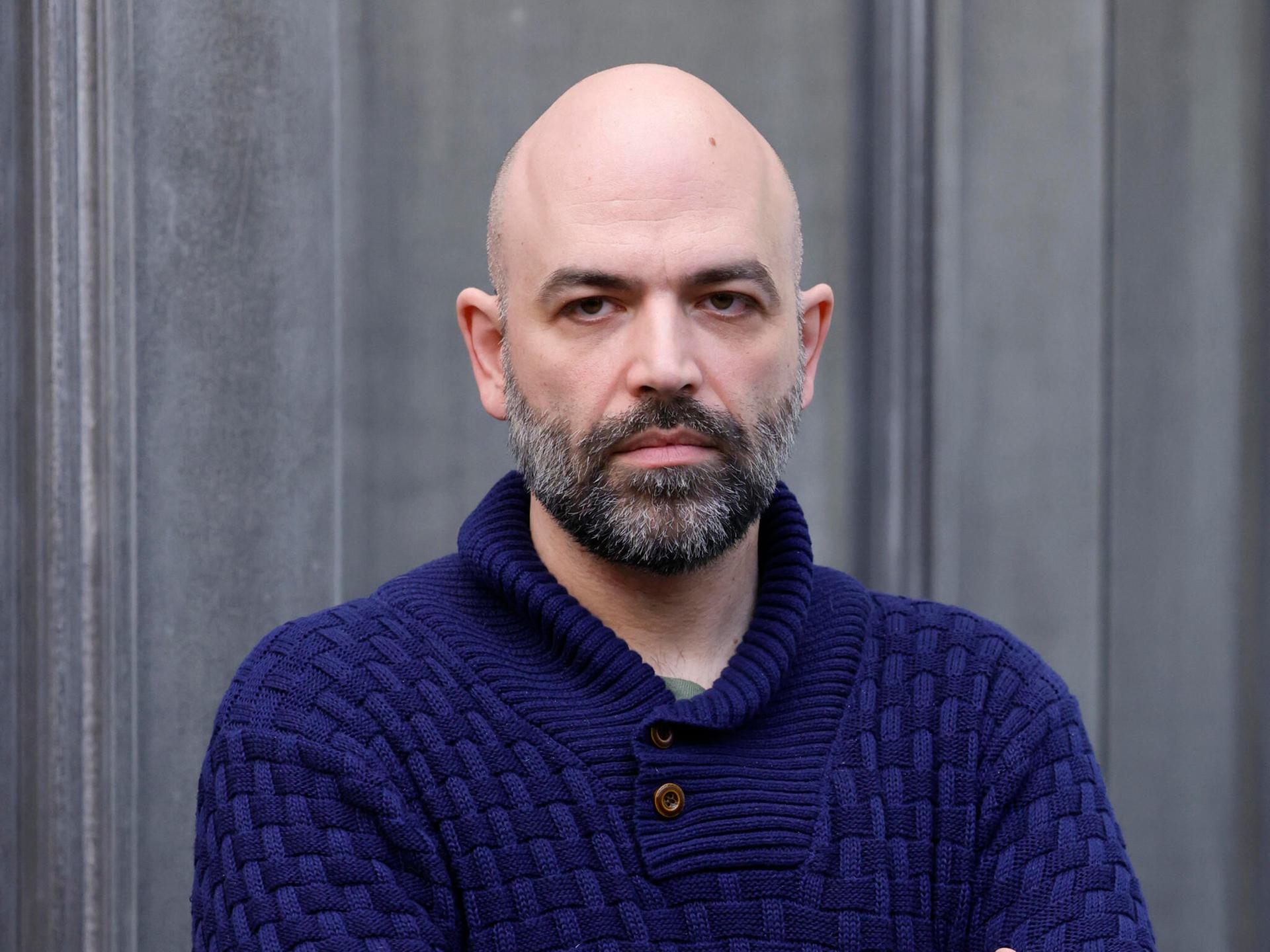 Der italienische Schriftsteller Roberto Saviano posiert für einen Fototermin. Er trägt einen dunkelblauen Wollpullover und verschränkt seine Arme.