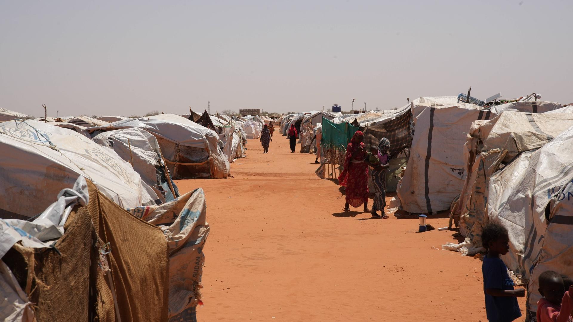 Menschen gehen zwischen Reihen provisorischer Unterkünfte in einem Flüchtlingslager in Al-Ubayyid, Nord-Kordofan, Sudan, hindurch.