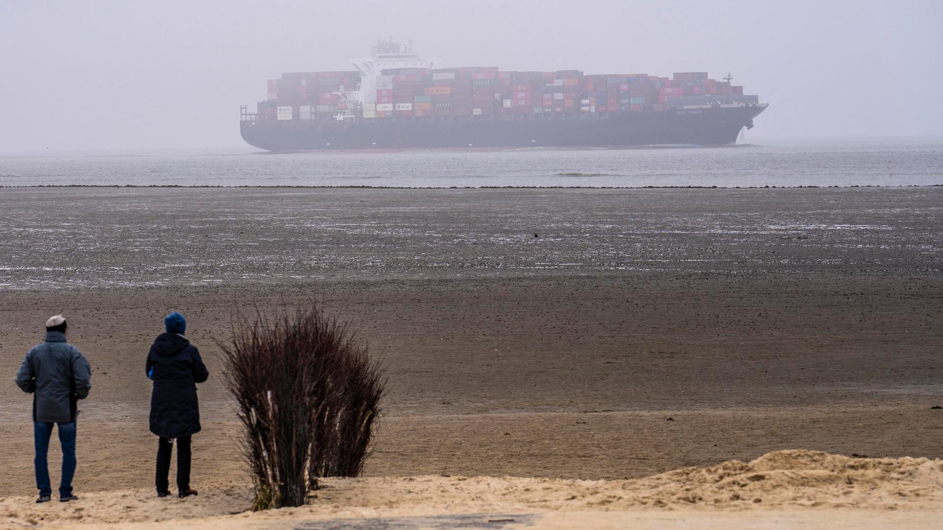 Das Containerschiff NYK Venus fährt bei dickem Nebel in die Unterelbe ein an der Mündung zur Nordsee in Cuxhaven ein - Menschen beobachten das Schiff