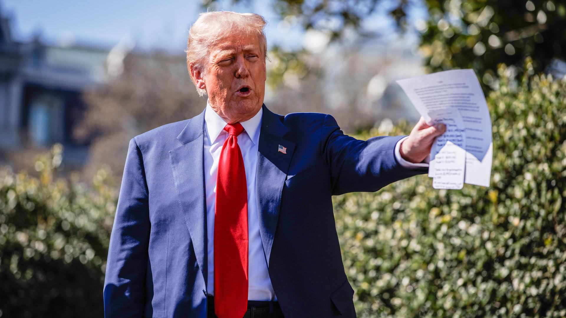 US-Präsident Donald Trump steht im Freien und spricht. Der linke Arm ist ausgestreckt, in der Hand hält er ein Text-Blatt.