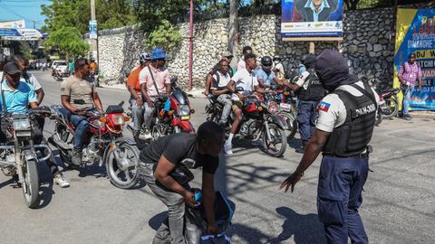 Haiti: Polizeibeamte kontrollieren Mopedfahrer auf Waffen. 