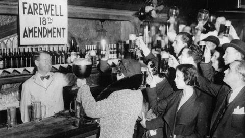 Schwarz-weiß Foto: Menschen stehen an einem Tresen und halten Biergläser in die Höhe. 