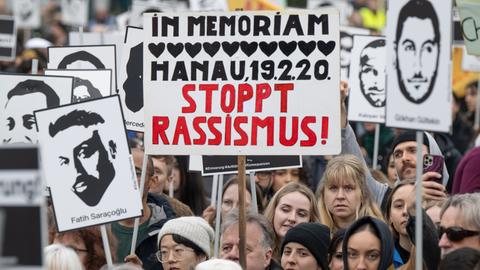 Mehrere tausend Menschen versammeln sich nach einem Gedenkmarsch anlässlich des vierten Jahrestages des rassistische Anschlags von Hanau auf dem Marktplatz in der Innenstadt. Viele Teilnehmer halten dabei Schilder und Bilder der Opfer hoch.