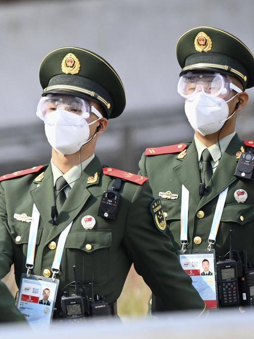 Drei Polizisten der Volksrepublik China marschieren durch einen Veranstaltungsort der Olympischen Winterspiele 2022 in Peking. Sie tragen grüne Uniformen und weiße Masken.
