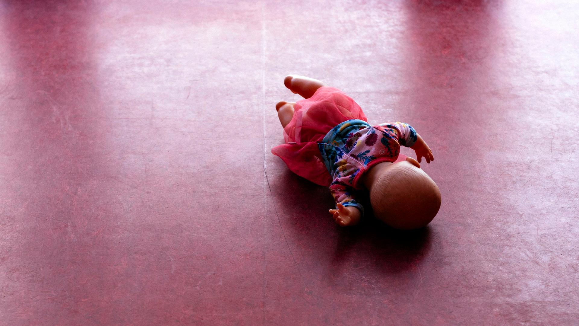 Eine Spielzeugpuppe liegt auf einem PVC-Fußboden.