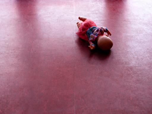 Eine Spielzeugpuppe liegt auf einem PVC-Fußboden.