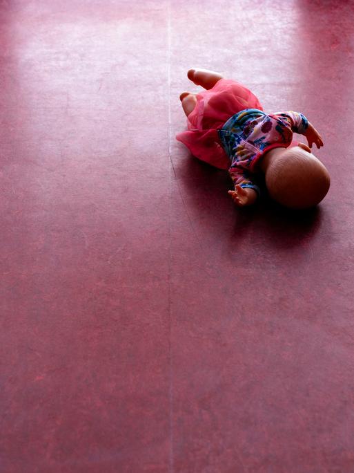 Eine Spielzeugpuppe liegt auf einem PVC-Fußboden.