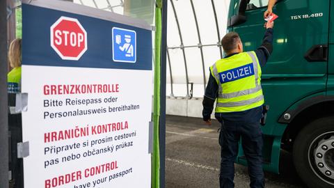 Ein Bundespolizist kontrolliert an der deutsch-tschechischen Grenze den Grenzverkehr, aus einem Lastwagen werden Dokumente zu ihm heruntergereicht.