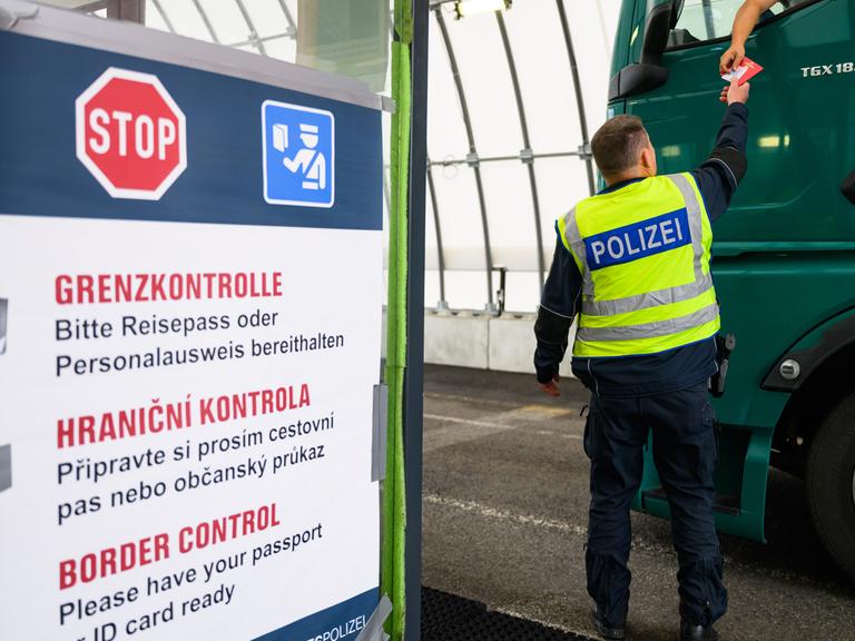 Ein Bundespolizist kontrolliert an der deutsch-tschechischen Grenze den Grenzverkehr, aus einem Lastwagen werden Dokumente zu ihm heruntergereicht.