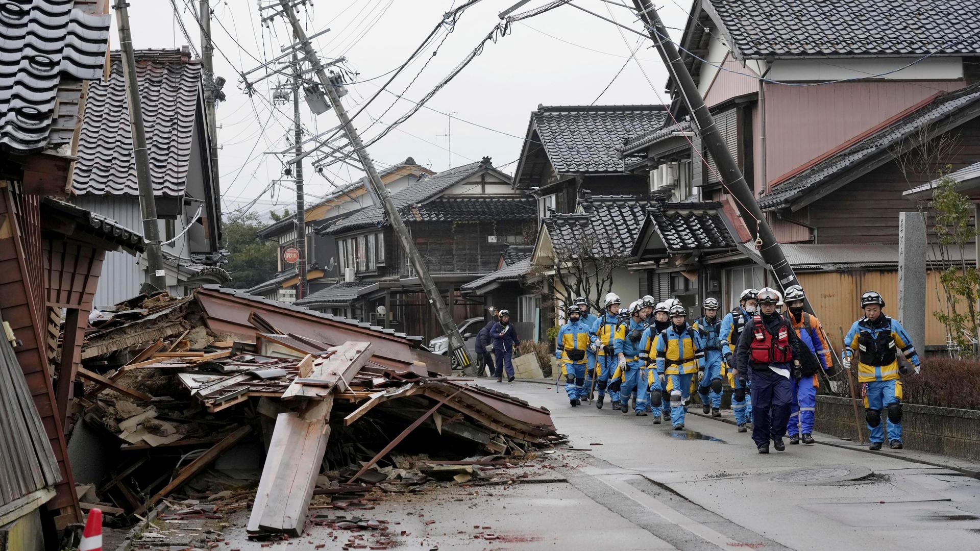 Japan, Suzu: Polizisten gehen an eingestürzten Häusern vorbei, die von den Erdbeben in Suzu, Präfektur Ishikawa getroffen wurden. Schlammlawinen und aufgerissene Straßen behindern die Suche nach Überlebenden.