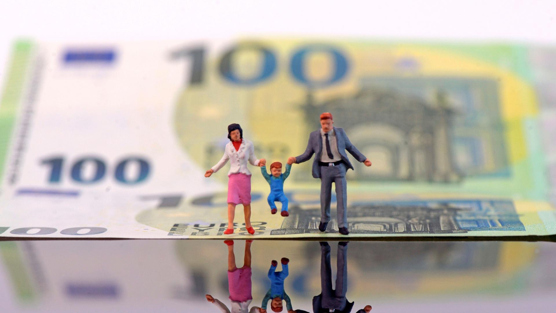 100 Euro-Schein mit kleinen Miniatur-Figuren davor, die Vater, Mutter und Kind darstellen. 100 Euro-Schein mit kleinen Miniatur-Figuren davor, die Vater, Mutter und Kind darstellen.