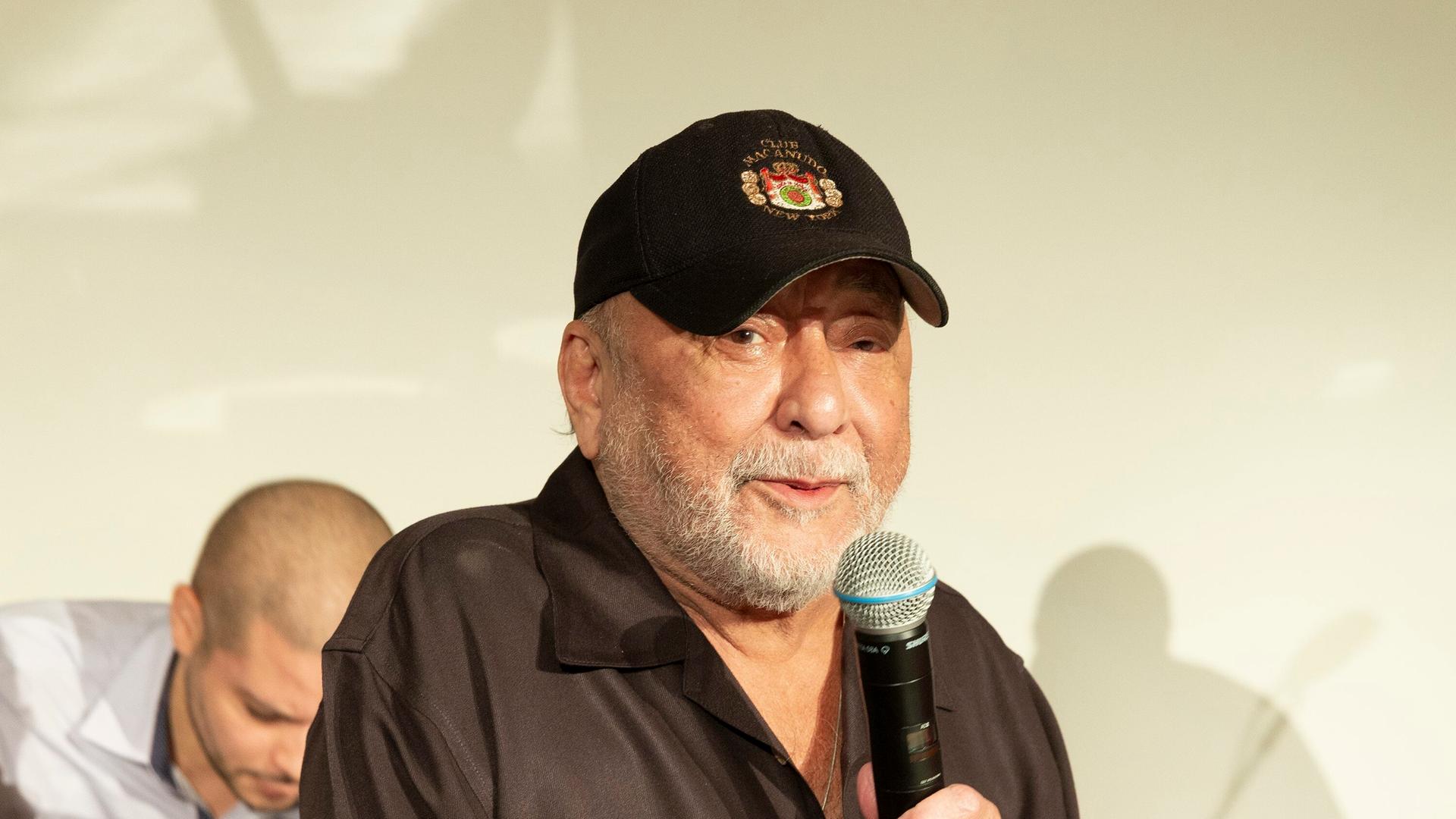 Eddie Palmieri trägt eine Baseballkappe und hält ein Mikrofon. Eddie Palmieri trägt eine Baseballkappe und hält ein Mikrofon.