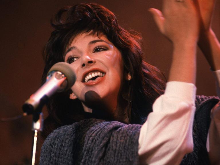 Kate Bush steht lächelnd an einem Mikro.
